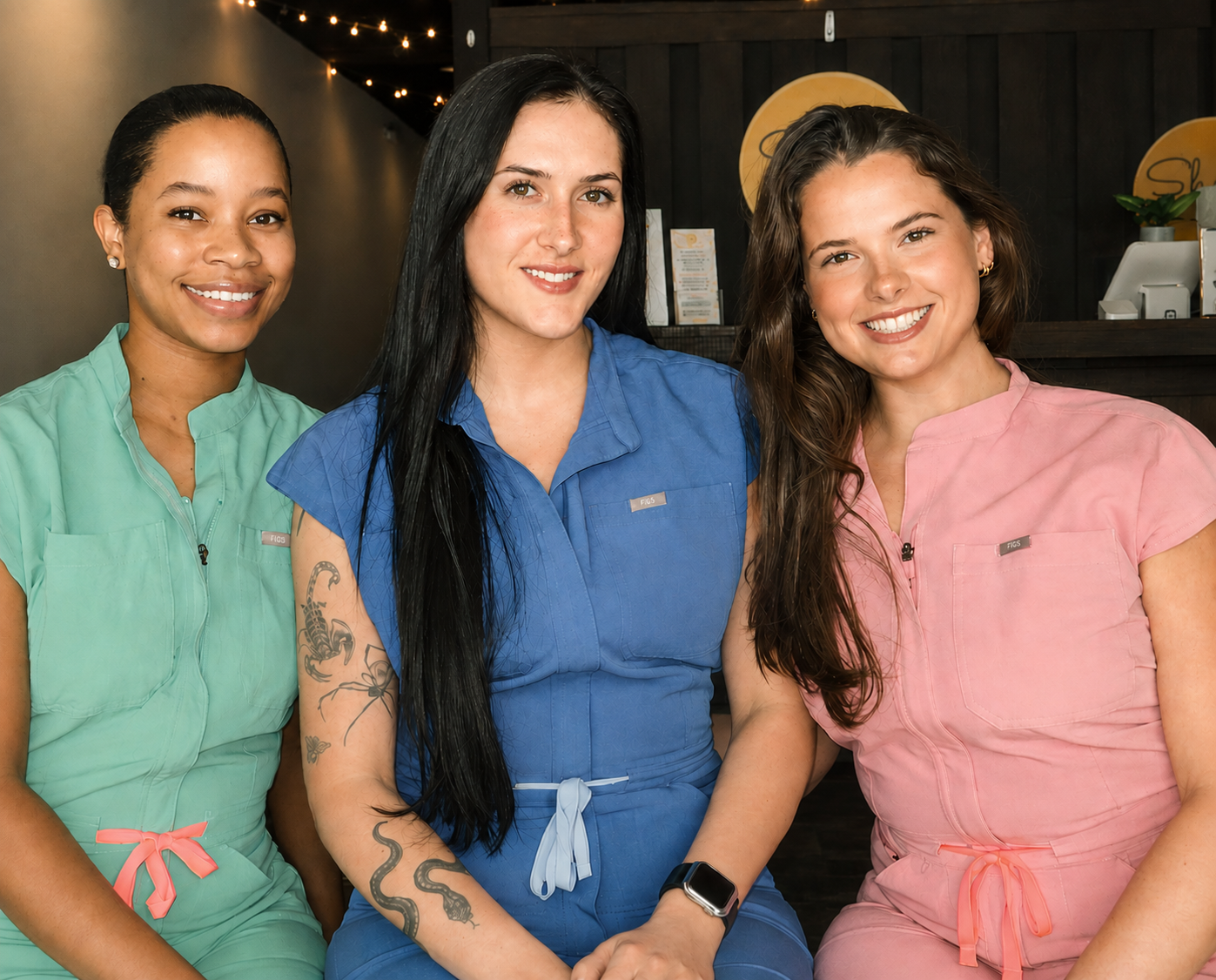 Three Shine Auburn estheticians in colorful scrubs smiling together in the studio lobby